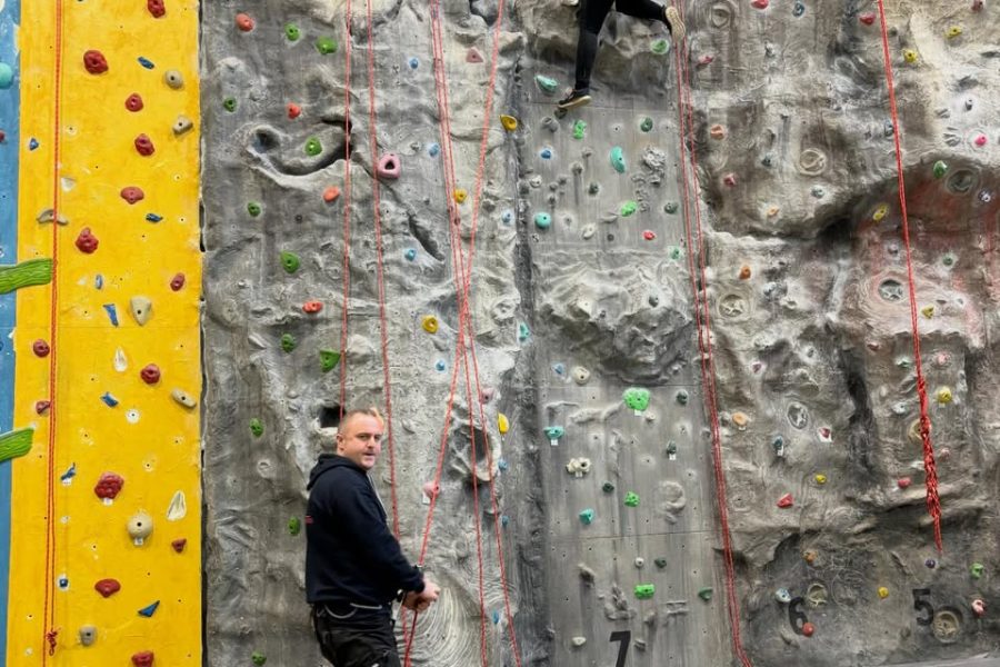 Picture of a young person on a climbing wall with an instructor below. Plus logo of South Coast Adventures