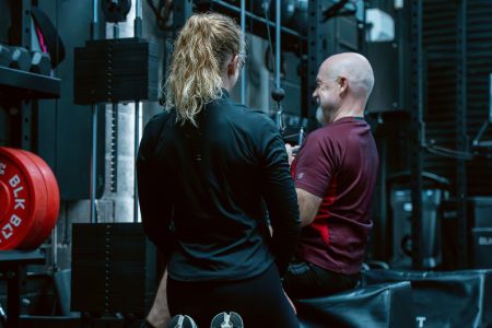 Photograph of trainer and client using some gym equipment. Plus Square One Gym logo