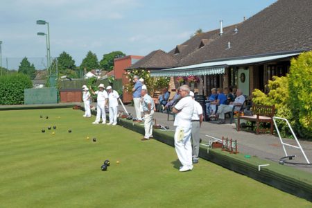 Photograph of a group go players in their whites on a bowling green enjoying a match. Plus Wimborne Bowls Club logo.