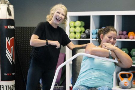 Photograph of a female trainer and client exercising with smiles on their faces. Plus WOW Logo