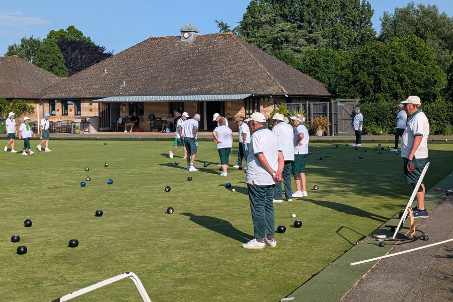 Photograph of Bowls Club Members playing the green with the Clubhouse in the background. Logo Of Wimborne Bowls Club