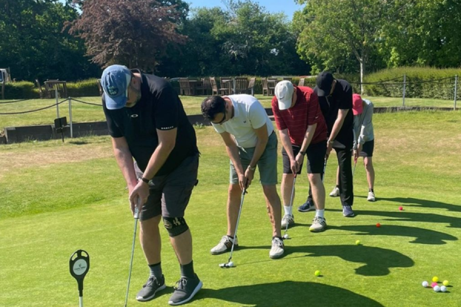 Five people in a line on a golf course putting on a sunny day